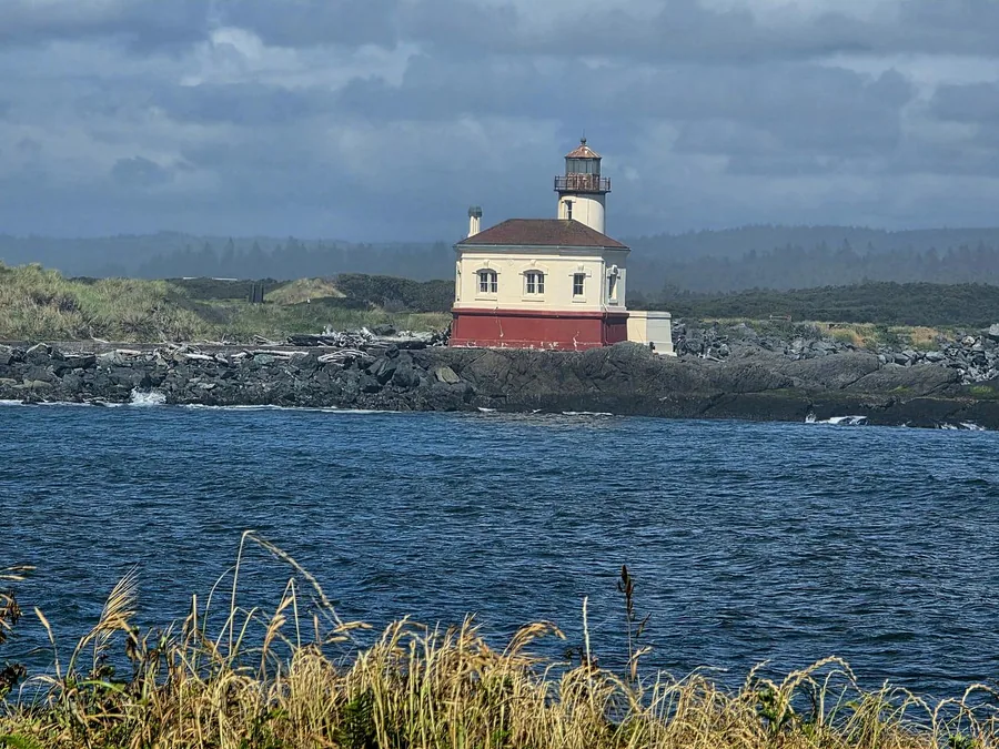 Coquille River Lighthouse on a stormy day, the Bandon coastline behind it