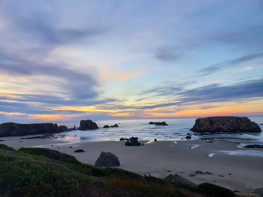 Bandon Beach at golden hour with sea stacks scattered along the shoreline and the long shadow of the dunes stretching across wet sand