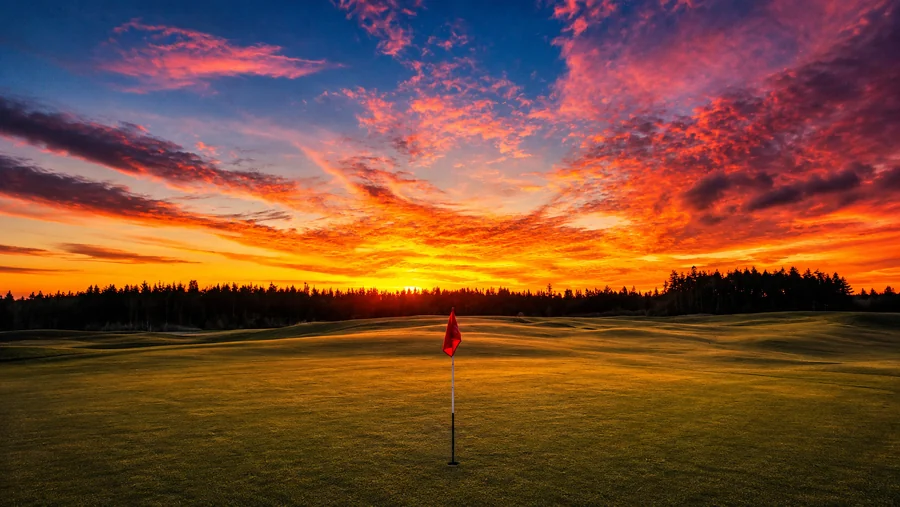 Sunset over a green at Bandon Dunes, a single flag on the putting surface beneath a fiery sky